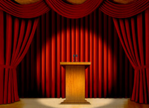 Podium,In,A,Spot,Light,On,Stage,Over,Red,Curtains.